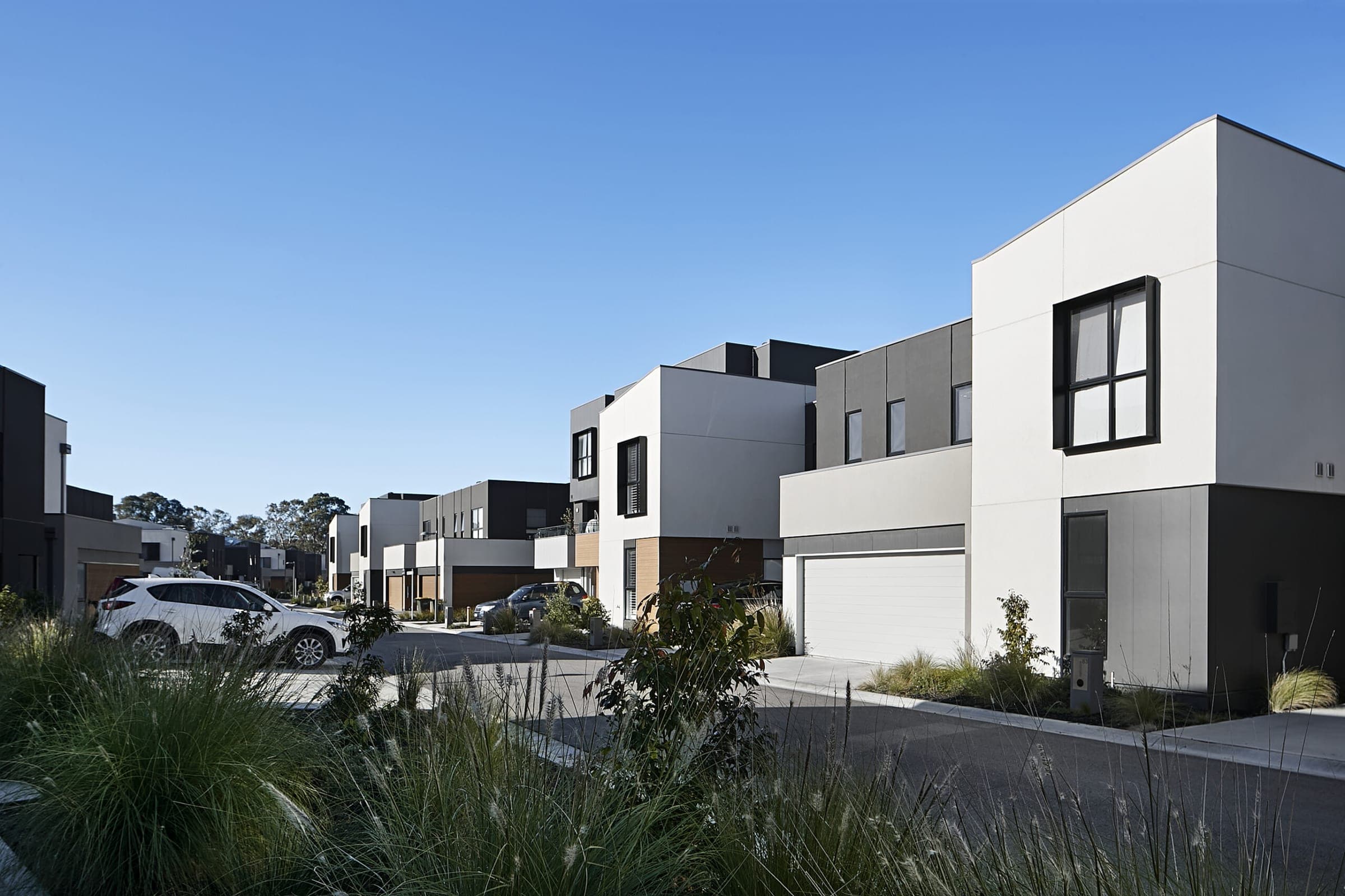 A completed XHomes townhouse street — white and charcoal facades under a clear sky